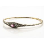 A Belle Epoque costume arm bangle, set with an oval pink paste stone, within a white metal setting