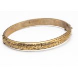 A 9ct gold hollow hinged bangle, oval shape with engraved floral decoration, interior measurements