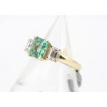 A three stone emerald and diamond 18ct gold dress ring, claw set square cut flanked by two