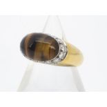An 18ct gold tiger's eye and diamond dress ring, the cabochon tiger's eye of oval design with a side