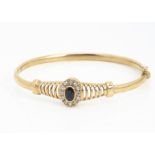 A gem set 9ct gold hinged bangle, with blue and white stones set in oval cluster with pierced
