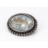 A 19th Century Indian miniature brooch, depicting a palace set within a lake, in white metal frame