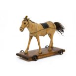 A carved wooden horse on wheeled platform, with glass eyes, fur mane and tail, oil cloth tack,