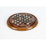 A late 19th century turned wooden solitaire board, with thirty three small glass marbles with