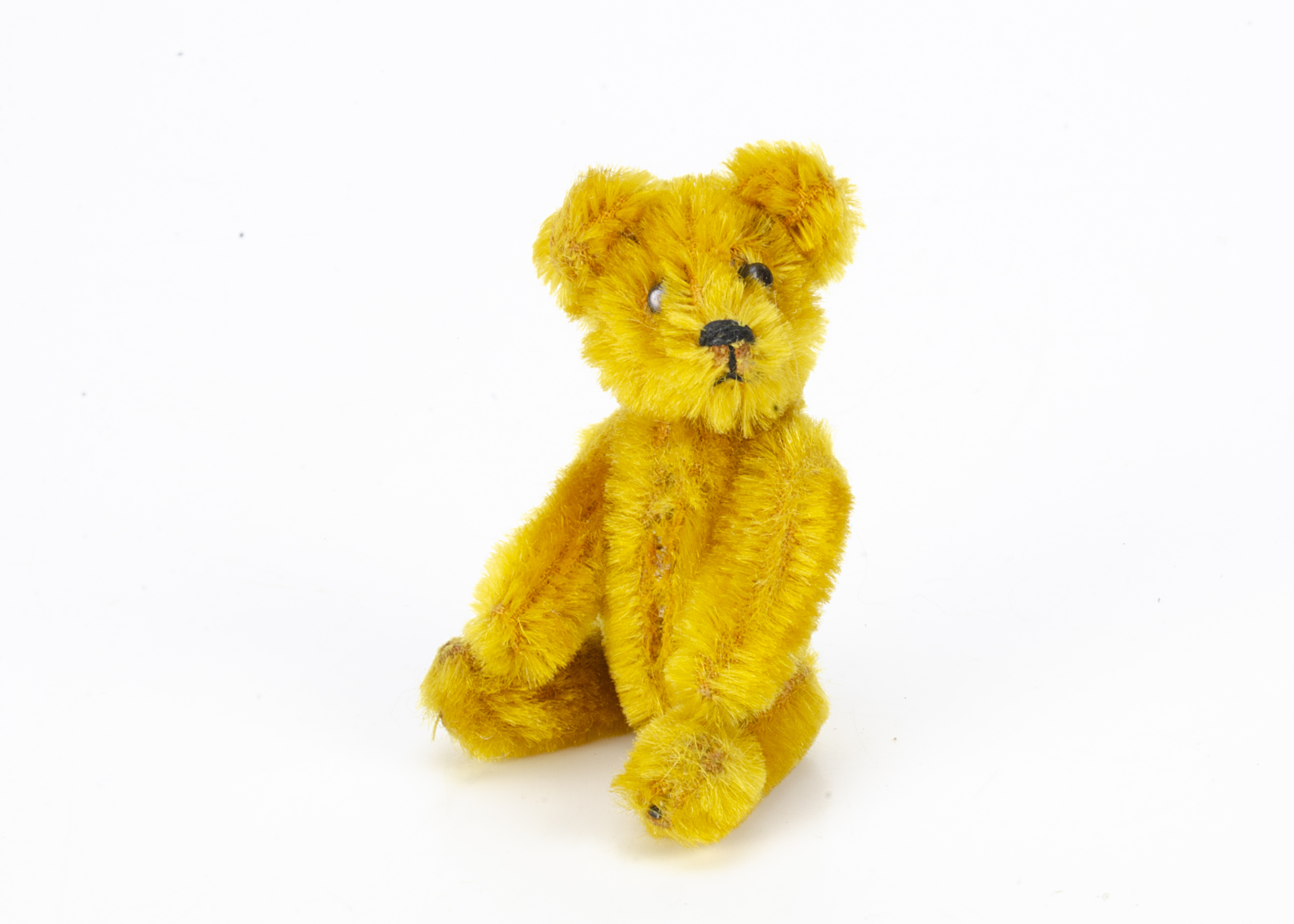 A Schuco miniature teddy bear 1950s, with golden mohair, metal eyes, black stitched nose and mouth