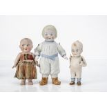 Three all-bisque comic children, the largest with moulded clothes, blue belt and shoes, blonde