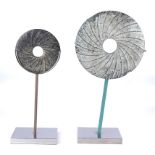 Two abstract stone disc forms on faux green and chrome type bases, diameter 21cm.