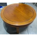 A contemporary oriental style hardwood table, circular grooved top, carving to frieze raised on