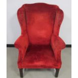 A Georgian style wing back arm chair, raised on square front reeded supports, upholstered in red