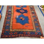 A 20th Century Caucasian rug, woven with repeating geometric designs, on a red ground, blue