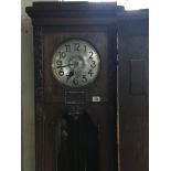A large oak long case clock with a silvered dial visible pendulum and weights.