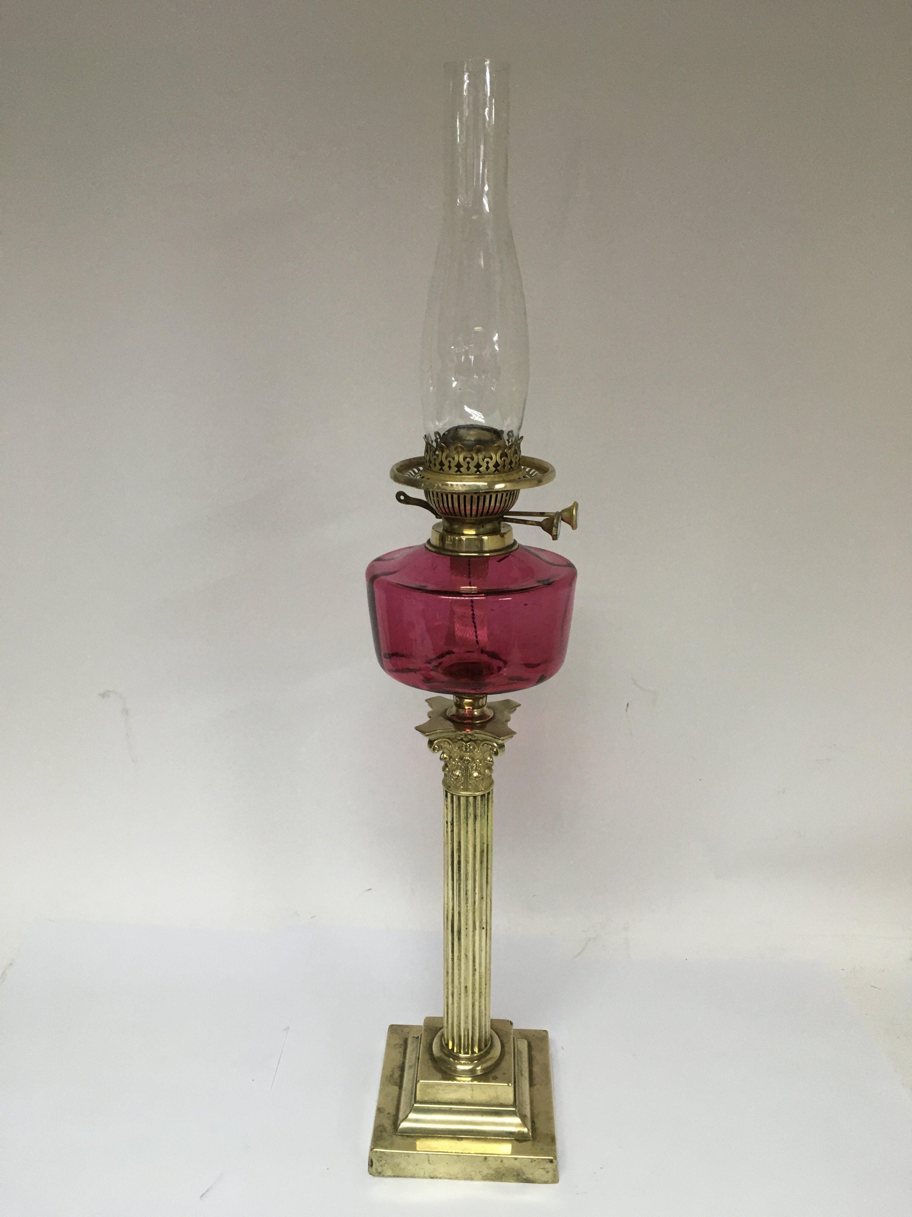 A brass oil lamp with a cranberry glass reservoir