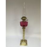 A brass oil lamp with a cranberry glass reservoir