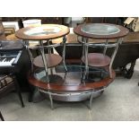 A group of three modern chrome and wooden tables with glass tops, including a coffee table and two