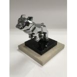 A small chrome car mascot of a Deco style dog, raised on a stepped base, approx height 10.5cm.