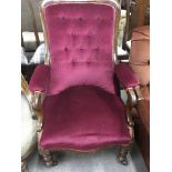 A Victorian mahogany button back open arm chair in red upholstery on turned legs .