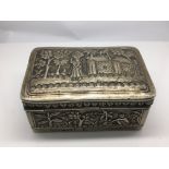 A small ornamental silver box decorated with figures in a garden setting.