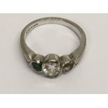 An 18ct white gold ring set with a single diamond flanked by emeralds, lacking one stone.Approx 5.