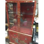 A Chinese style red lacquer cabinet with two glazed doors and cupboards under on a plinth base