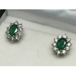 A pair of boxed emerald and diamond cluster studs.