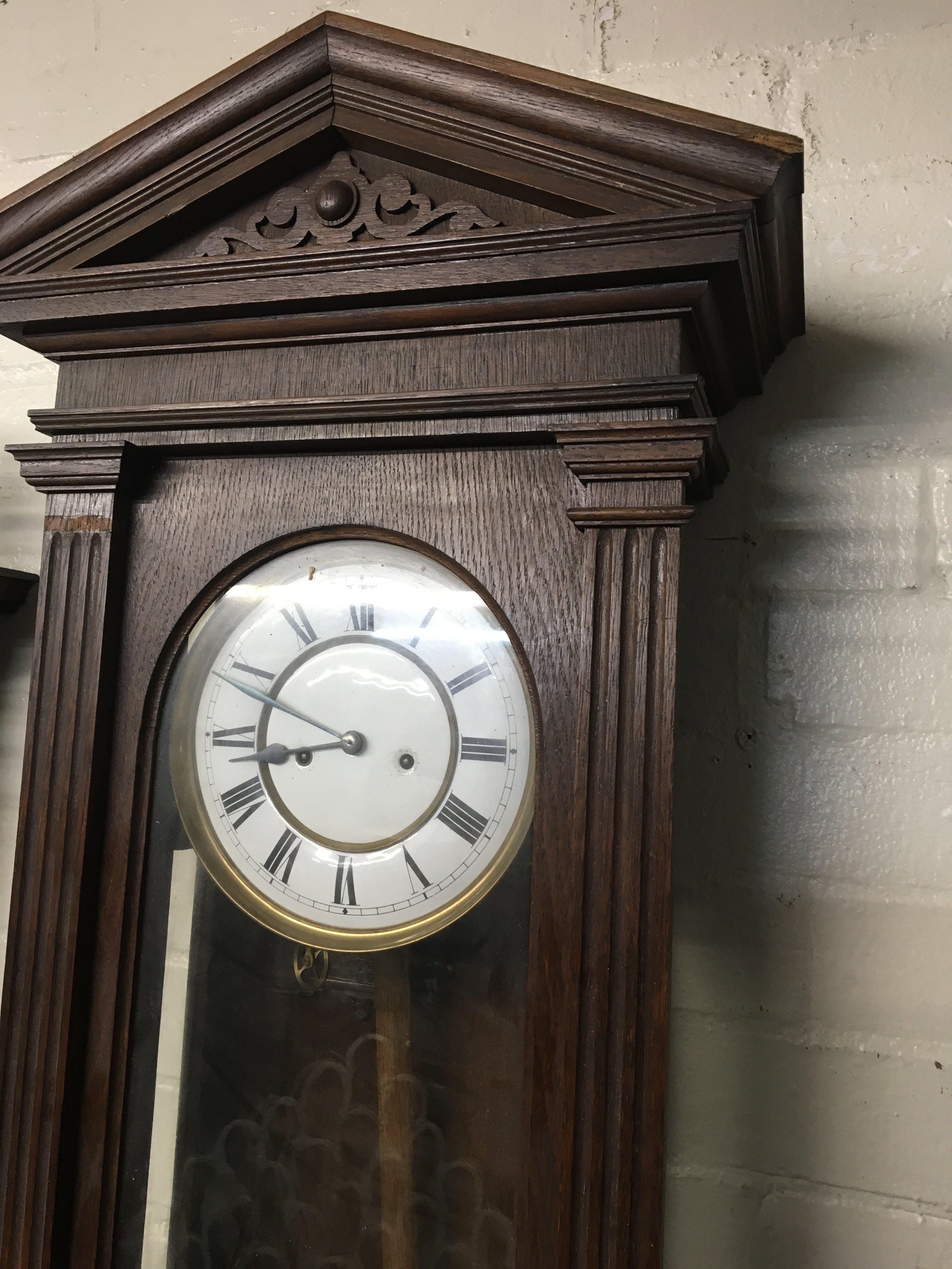 A walnut Vienna wall clock the dial with Roman numerals and visible pendulum.