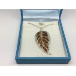A silver and amber pendant in the form of a leaf on a chain.