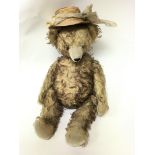 A large vintage plush teddy bear with long arms and straw hat and growler