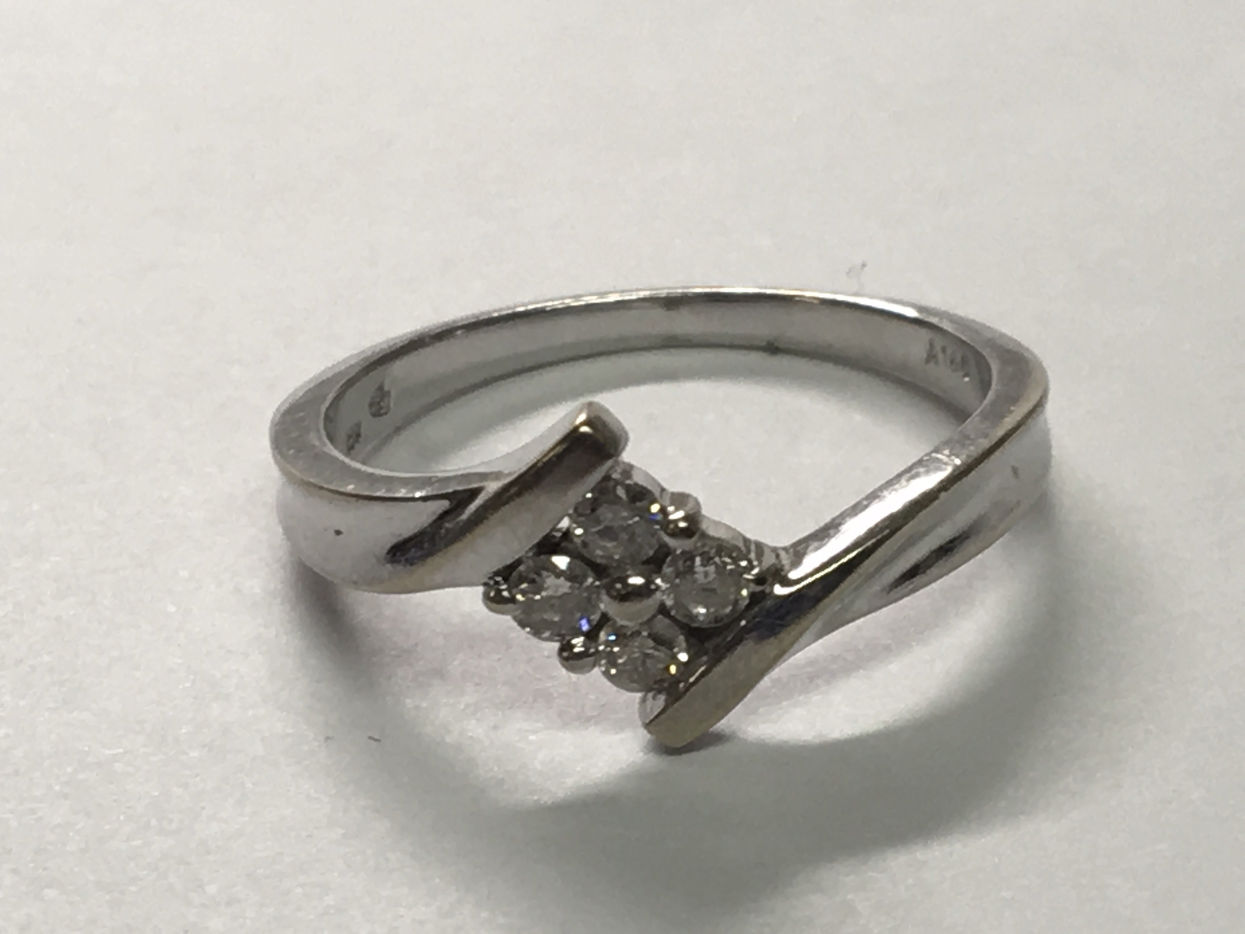 A ten carat white gold ring set with a pattern of four brilliant cut diamonds. ring size N