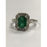 A platinum ring set with a 1.5ct square cut emerald surrounded by 0.5ct of diamonds, (L)