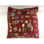 A red cushion with approx 50 brooches attached.