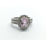 An unmarked white gold ring set with a central pink sapphire and surrounded by diamonds, approx 1/