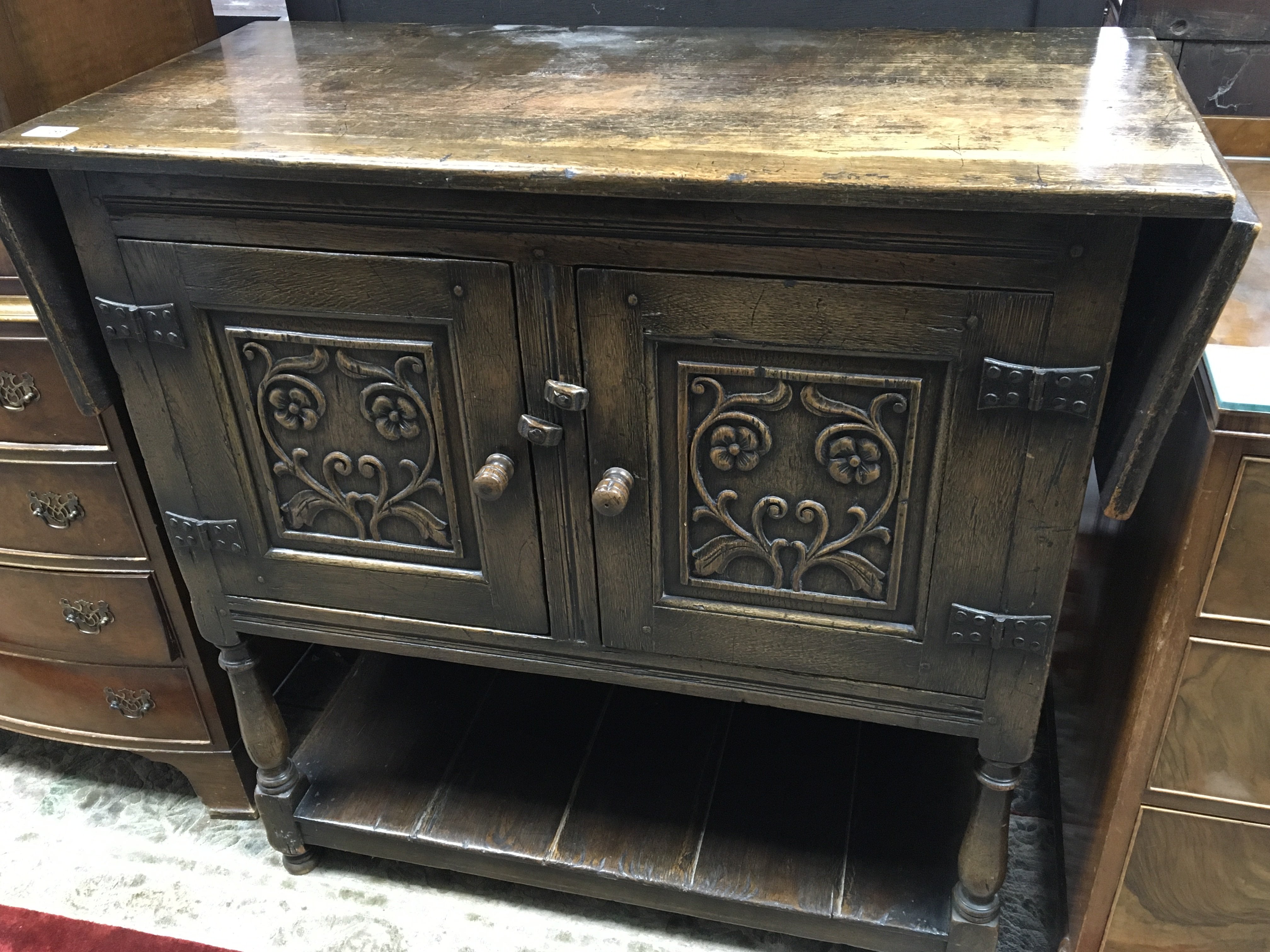 A carved oak cupboard the top with a drop flap abo