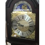 A reproduction mahogany longcase clock with visible pendulum and weights the dial with a moon