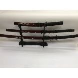 Three graduated reproduction Japanese swords on a