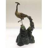 A bronzed figure of a peacock raised on a hardston