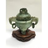 A carved jade incense burner raised on a hardwood