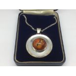 An amber and silver circular pendant on chain.