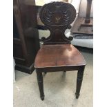 A late George III mahogany hall chair with a shaped back and decorated with a crest. damaged back