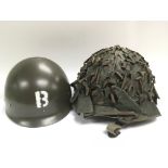 A vintage camouflage helmet stamped JAPY 1953 to the interior together with a reproduction