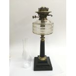 An iron Corinthian column oil lamp with a clear glass reservoir.