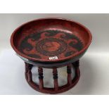 A large red and black painted Tibetan bowl on stand.