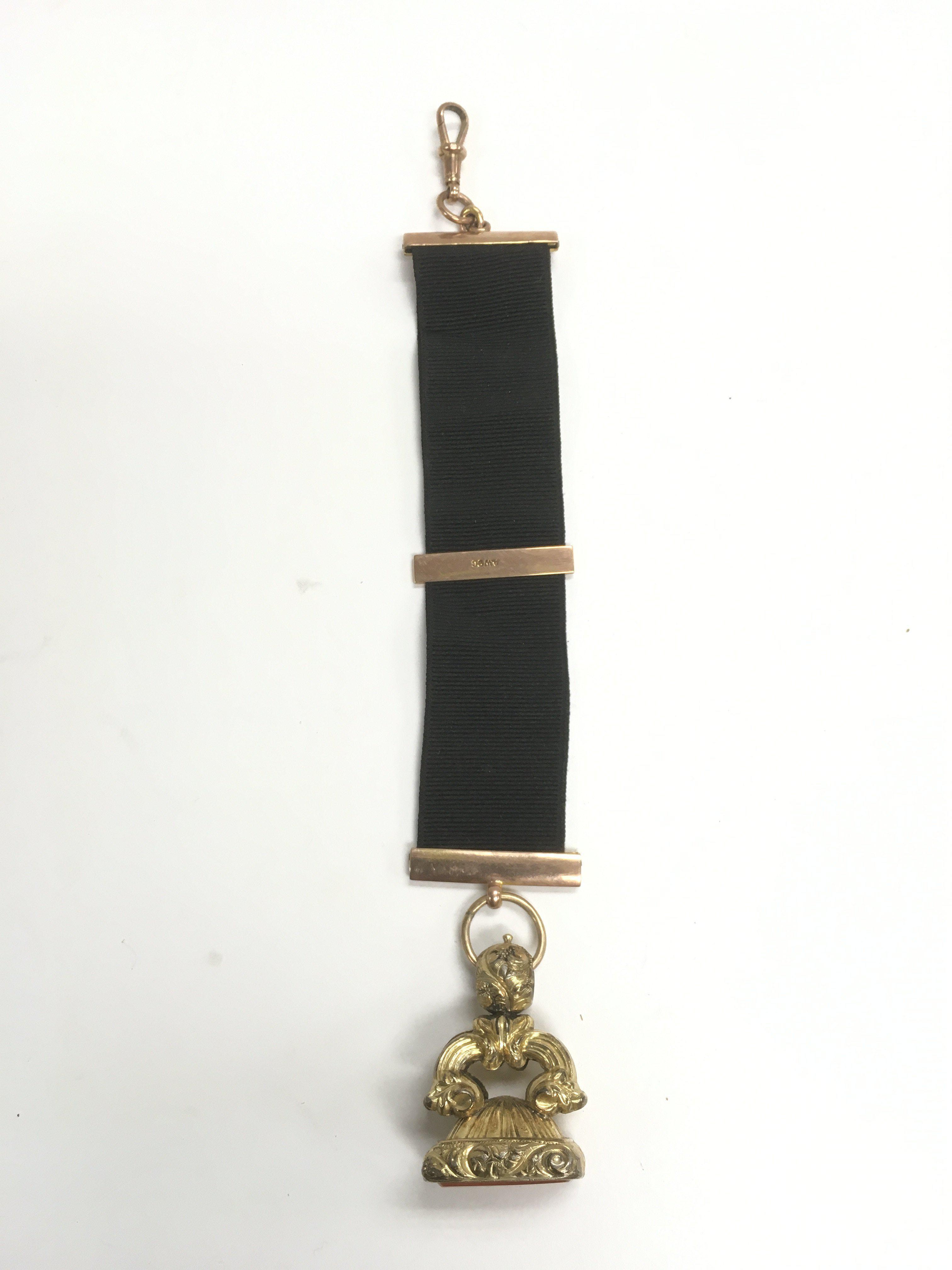 A seal fob suspended on a ribbon set with 9ct gold.