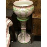An Edwardian ceramic jardiniere and pedestal decorated with garlands of flowers on a pale pink