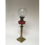 A Quality late 19th century brass corinthian column oil lamp with a cranberry glass reservoir and