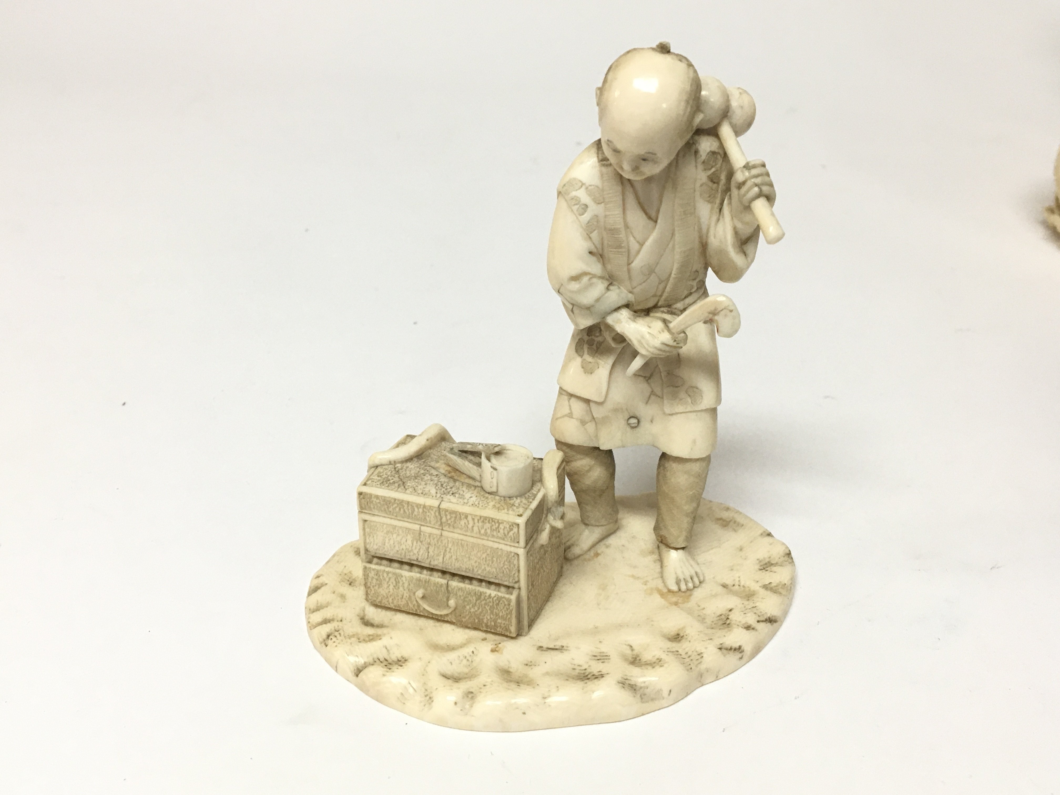 A late 19th century Japanese ivory carving of a craftsman with a chest of tools on a shaped base.