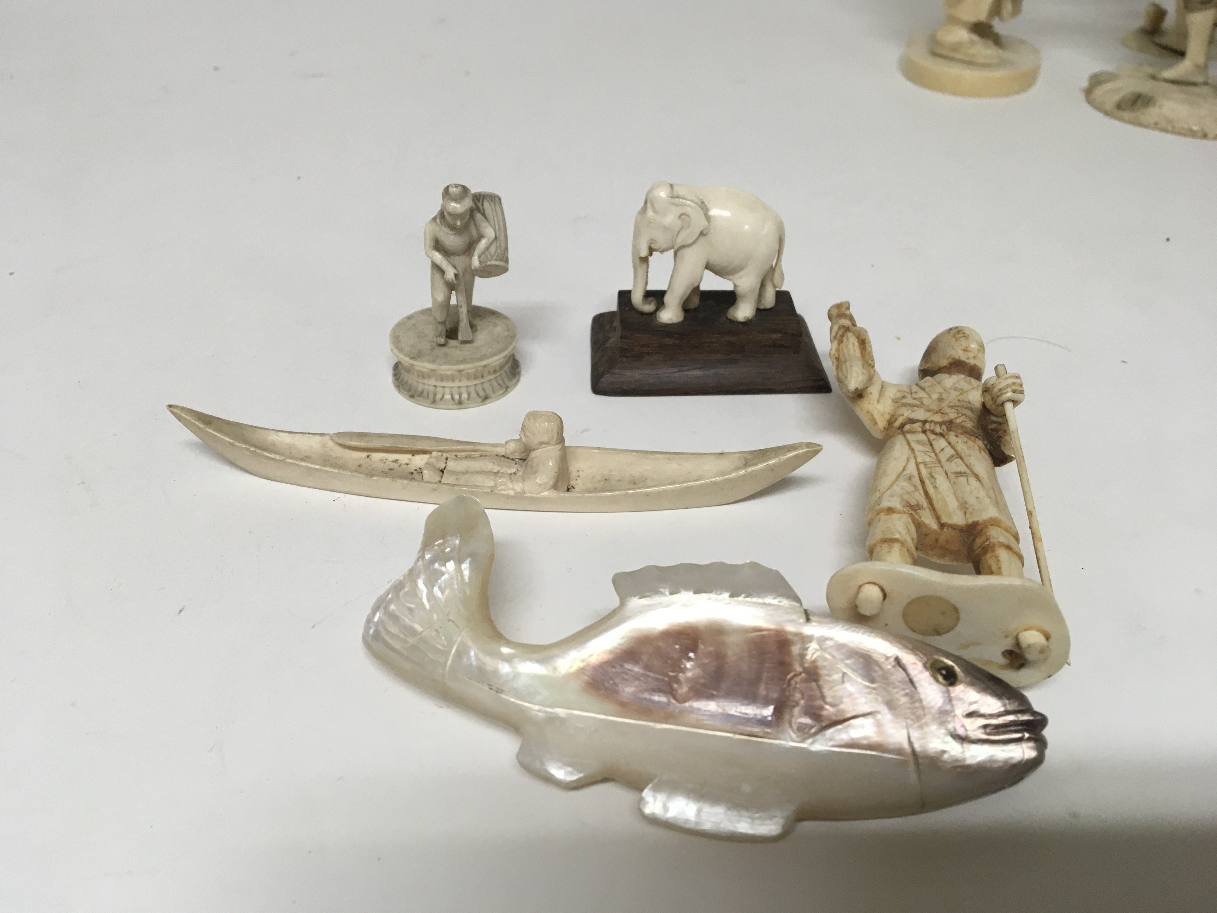 A collection of small carved ivory and bone figures and a mother of pearl carving in the form of a