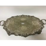 A large silver plated tea tray with a shaped edge and scroll feet diameter including handles 72cm