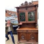 A book case cupboard profusely carved with a pair of lead light panels fitted with drawers and