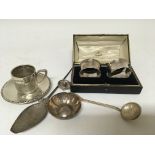 A collection of silver oddments a white metal South American spoon cup and saucer cased napkin rings