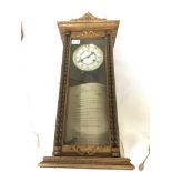 An oak wall clock Vienna type with visible pendulum.